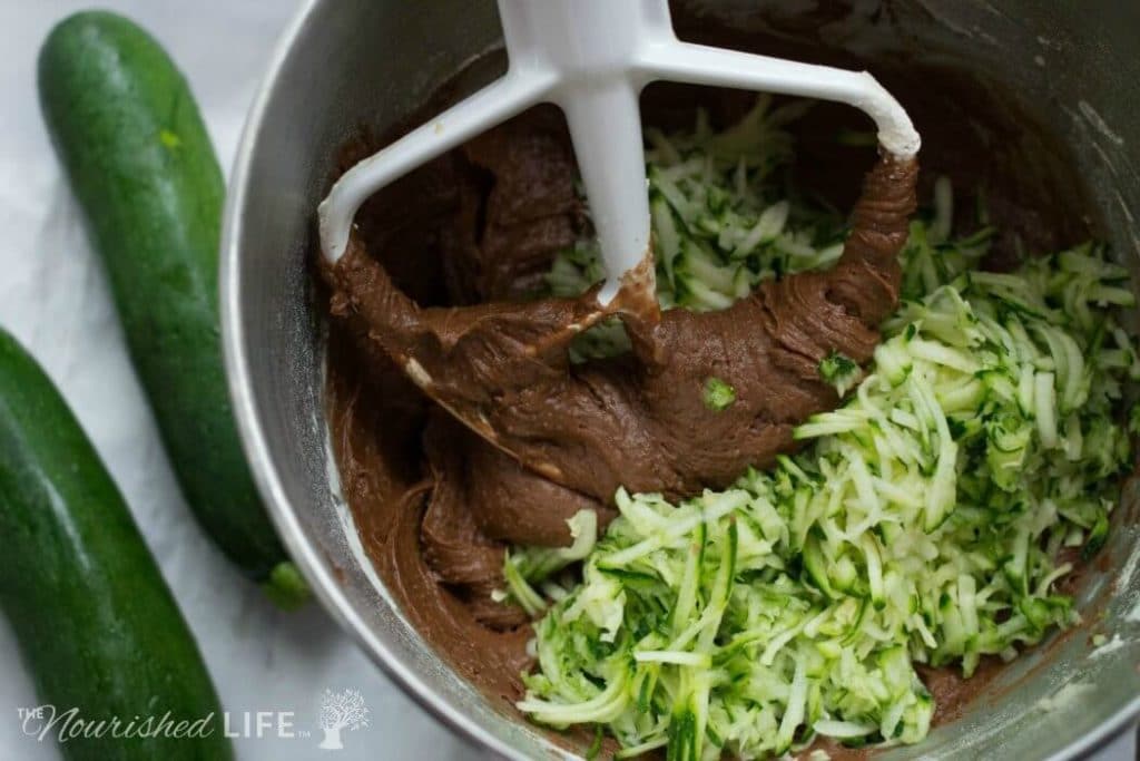 Chocolate batter in a stand mixer with shredded zucchini added for mixing