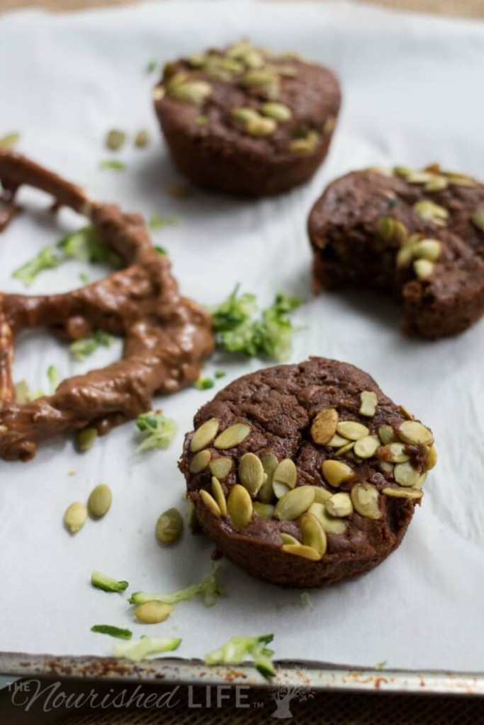 Three fresh baked chocolate zucchini muffins with pumpkin seeds on top